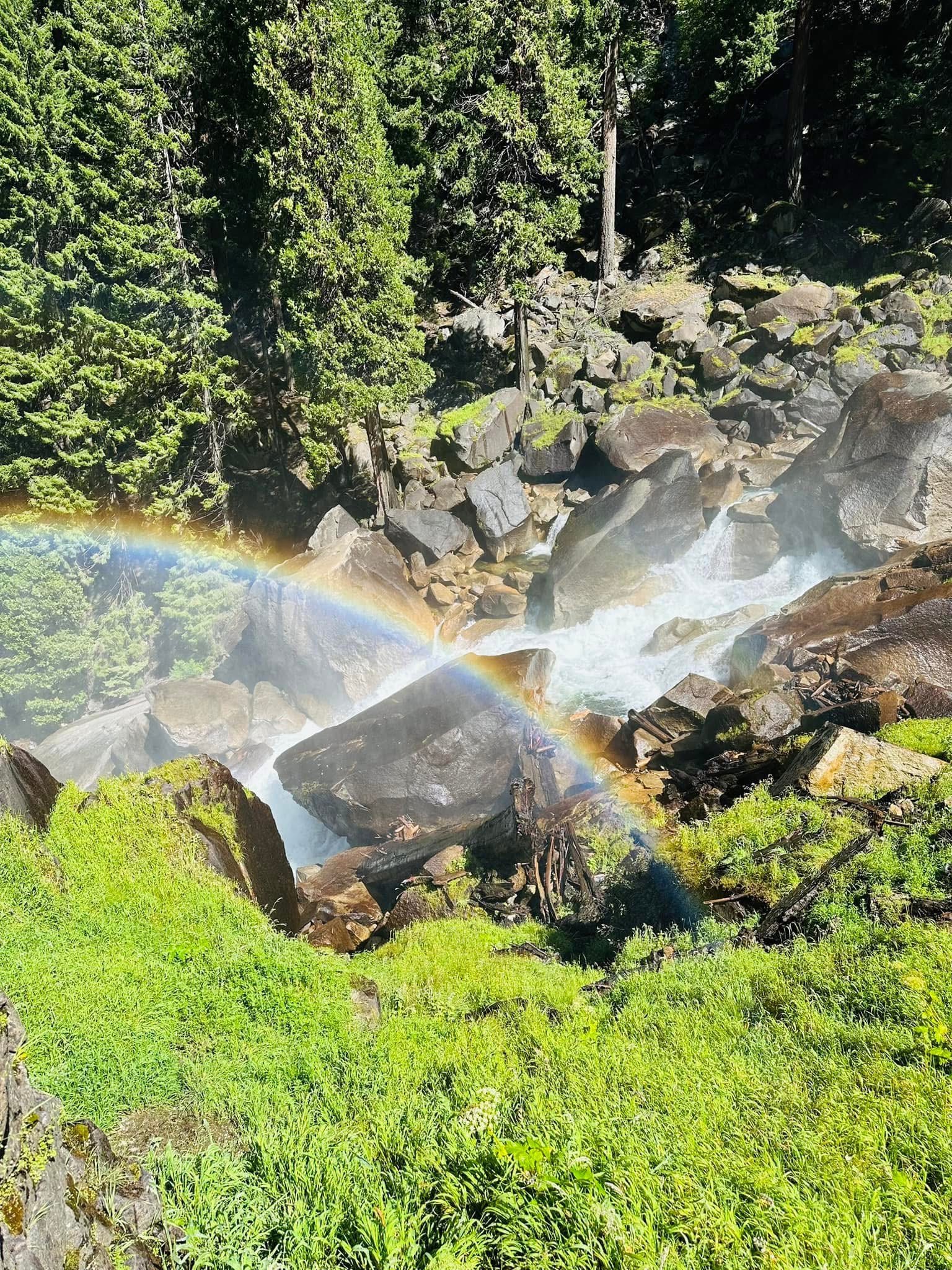 A waterfall with a rainbow arcing over green mountainside